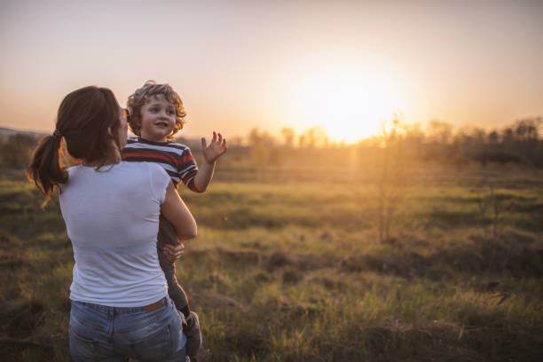 Mother and son enjoy on meadow at sunset