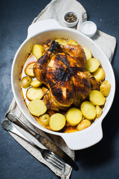 istock Baked whole chicken with potato garnish. Dark background, top view 1128165102