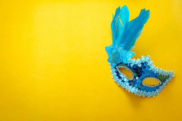 Photo of Table top view aerial image of beautiful colorful carnival season or photo booth prop Mardi Gras background.Flat lay object close up blue mask on modern yellow wallpaper.Free space for text mock up.