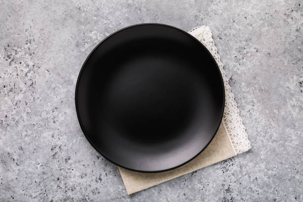 istock Empty ceramic plate in black with a napkin on gray concrete table, top view 1128171227