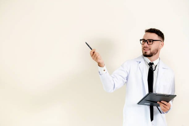 istock Male doctor points pen at empty copy space while holding a document clipboard in another hand. 1128171422