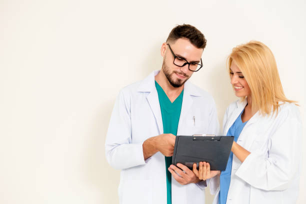 istock GP doctor looks at data in documents on clipboard while discussing with surgical doctor on white background. Medical service and healthcare concept. 1128172132