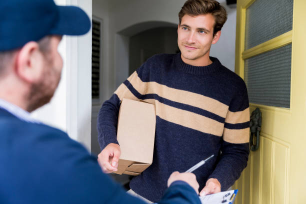 istock Man holding box while looking at delivery person 1128175384