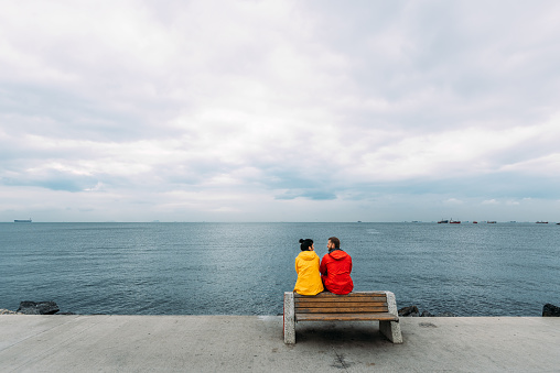 Young couple sitting on a bench by the sea. Man and woman traveling. People sit on a bench and look at the sea. Tourists by the sea. Friends on the bench. A lonely pair. Walking along the promenade