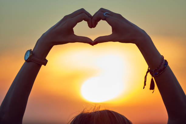 menina segurando o símbolo do coração-forma de amor no pôr do sol / nascer do sol tempo. - heart shape loneliness women praying - fotografias e filmes do acervo