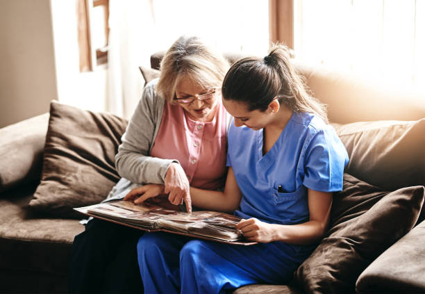 Triggering some old memories Shot of a nurse and a senior woman looking at a photo album together nursing home photos stock pictures, royalty-free photos & images