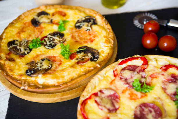 istock Two Pizza on white wooden table and black stone surface. Ready to eat 1128184599