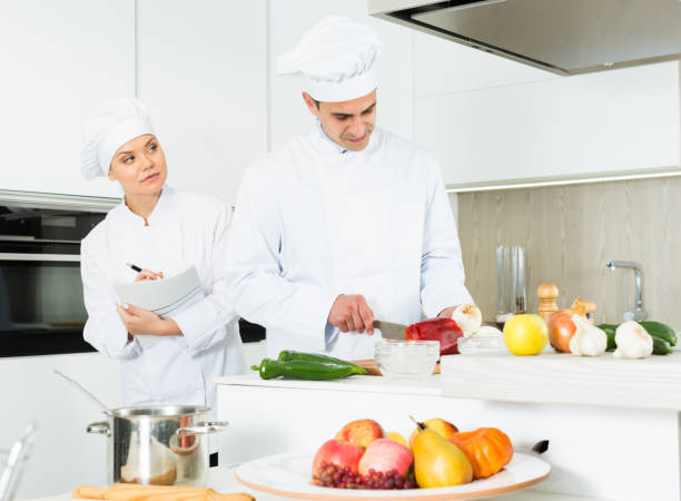 istock Chefs  in uniform  prepare vegetables with paper recipe on kitchen 1128189076