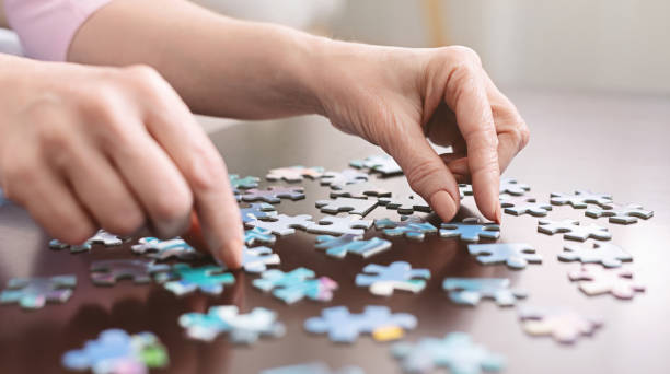 Elderly woman hands doing jigsaw puzzle closeup Dementia prevention. Elderly woman hands doing jigsaw puzzle at home, panorama, close up mental health photos stock pictures, royalty-free photos & images