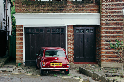London, UK - July 30, 2018: Red oldstyle Mini parked in front of the garage of the typical brick terraced house in London, UK