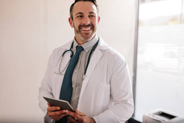 medico maschio maturo con un tablet digitale nel suo ufficio - doctor male doctor mature men portrait foto e immagini stock