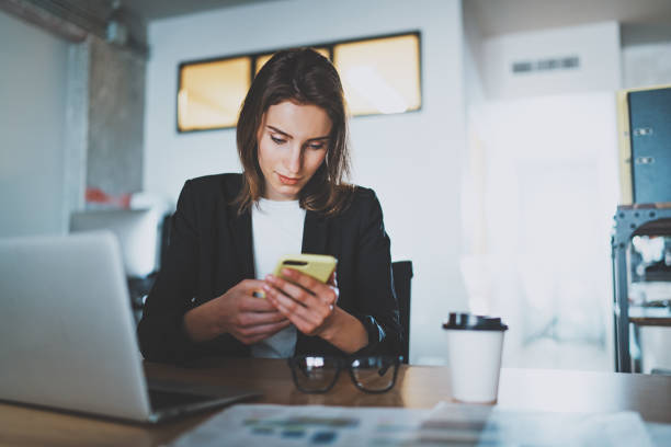 istock Smiling young businesswoman typing text message on smartphone while working at office.Blurred background. 1128195953