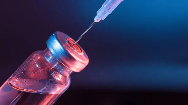 Injection vial with syringe needle on blue background.
