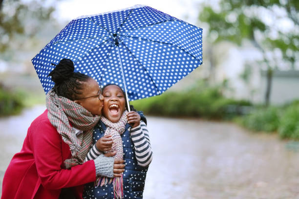 Rain won't spoil our day Shot of woman kissing her daughter under an umbrella below stock pictures, royalty-free photos & images