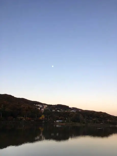 The moon is floating in the sky above the village with a calm lake.
