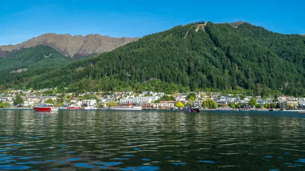Photo of Queenstown lakefront city center shot at Lake Wakapitu, the famous lake of Queenstown, center of tourism, water sport and boat tours, South Island of New Zealand.