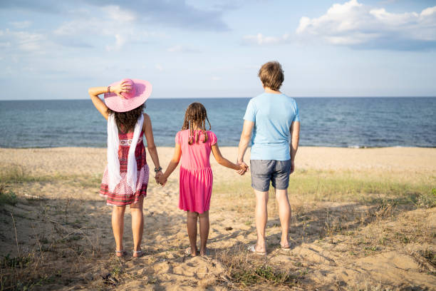 Rear view of family enjoying summer vacations on beach, holding hands and having fun.