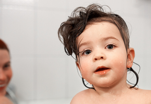 portrait of adorable baby girl with wet hair looking at camera, mother laughing in background.