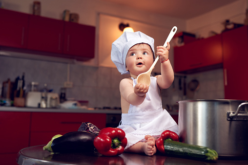 cute little girl in the kitchen, surrounded by fresh vegetables, playing with spoon.