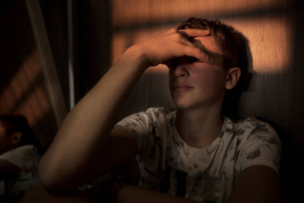 Teenager Boy Under Stress portrait of a teenager boy sitting in the dark room, with a beam of light over his eyes teenage boys stock pictures, royalty-free photos & images