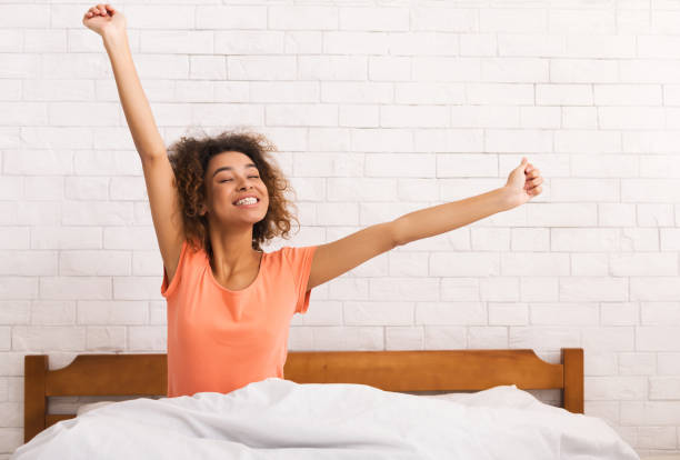 african-american woman stretching, sitting on bed in morning - wake up stretching women black imagens e fotografias de stock