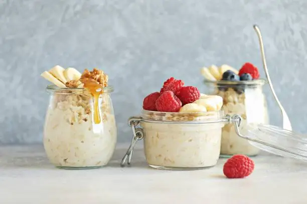 Overnight oats with fresh raspberry, banana and honey. Healthy breakfast in glass jars.