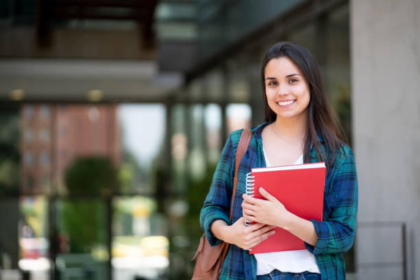 istock Young female student at university campus holding her notebooks while smiling at camera 1128235762