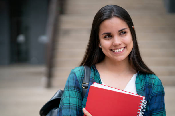 istock Latin american young student at college campus looking away thoughtful but happy while holding her notebooks 1128235787