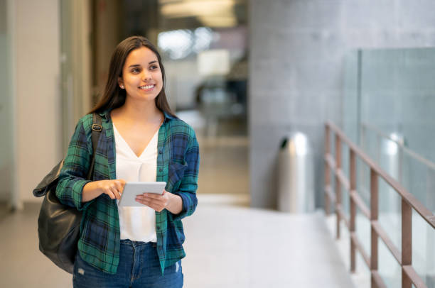 Beautiful college student walkign towards class holding her tablet looking away daydreaming
