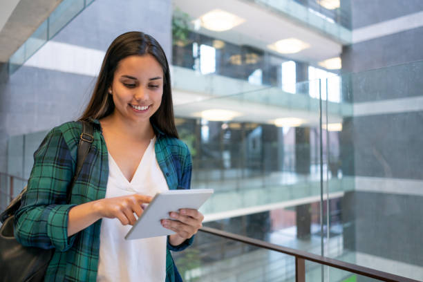 istock Beautiful young student at the college building looking at something on tablet smiling 1128235798