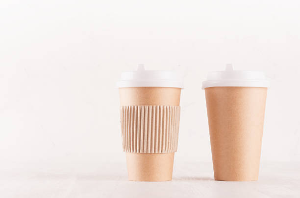istock Coffee packing mockup -  two craft brown paper cups with white cap, kraft cup holder on white wood board with copy space, coffee shop interior. Modern elegant concept for branding identity, advertising, design. 1128236999
