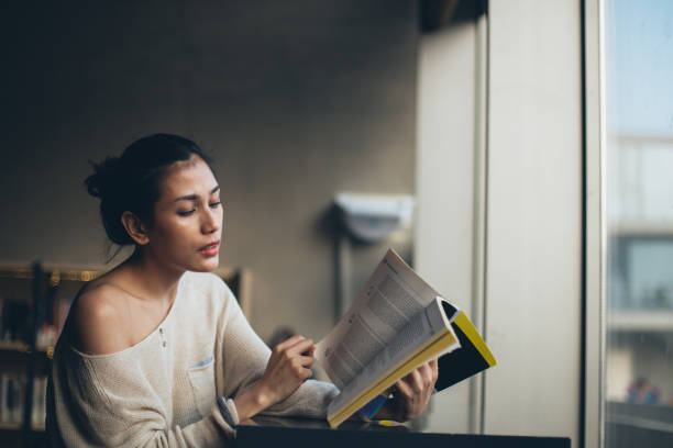 istock Beautiful woman reading a book in library 1128238385