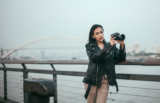 One woman, standing by the river, taking photos with a camera.