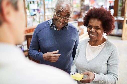 Senior couple purchasing medicine at pharmacy. African senior man and woman talking with pharmacist while buying their medicine.