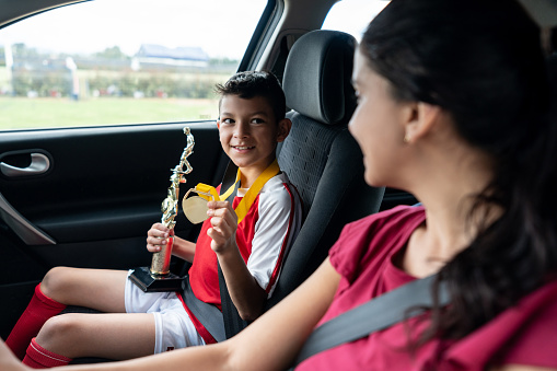 Happy boy in the car showing his soccer mom the trophy he won in summer camp