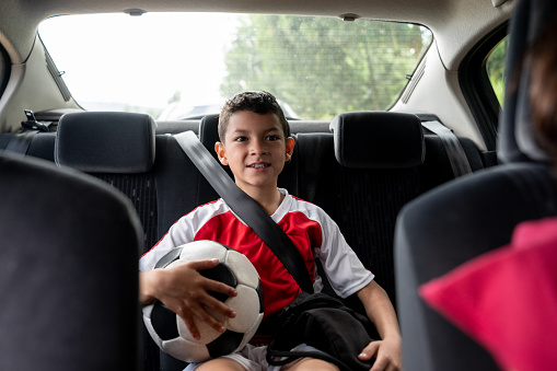 Portrait of a happy boy in a car on his way to football practice holding a ball and smiling â lifestyle concepts