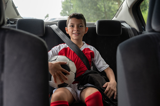Portrait of a happy boy in a car on his way to soccer practice holding a ball and smiling â lifestyle concepts