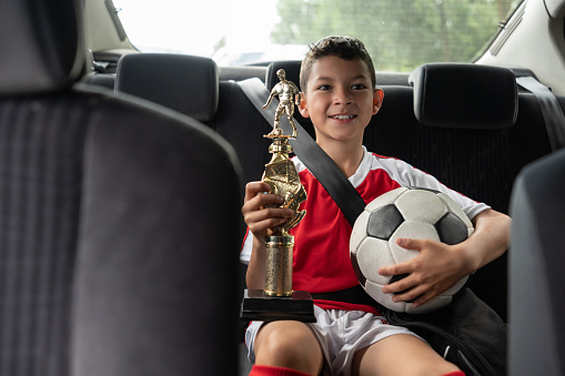 Portrait of a boy in the car after soccer practice looking happy holding his trophy and smiling