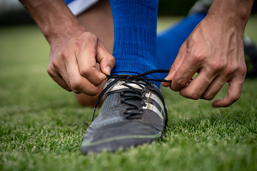 Close-up on a soccer player kneeling down tying his shoelace on the football field â sports concepts