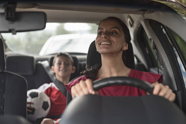 happy soccer mom transporting kid to football practice in her car - praticar imagens e fotografias de stock