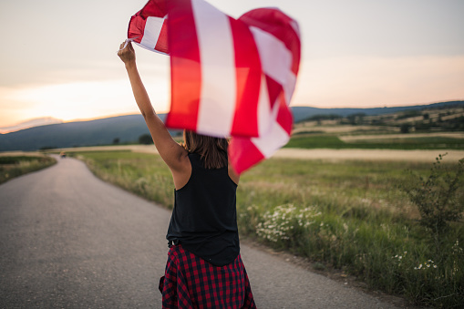 One woman, standing on the street in nature, holding US flag, rear view.