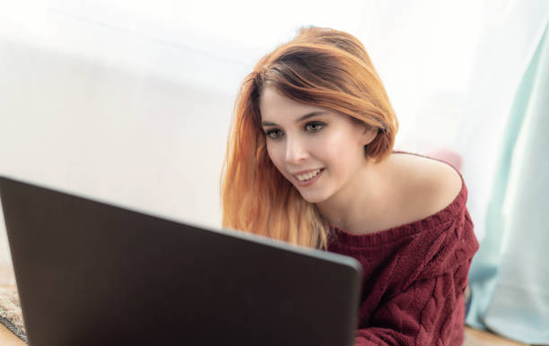 istock Attractive woman using a laptop laying on the floor, looking into webcam 1128247182
