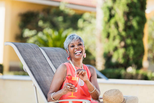 Senior African-American woman relaxing with tropical drink A senior African-American woman in her 70s relaxing on a pool deck in a lounge chair, enjoying a tropical drink. drinks on the deck stock pictures, royalty-free photos & images