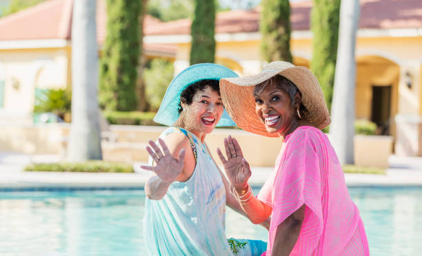 istock Two senior women sitting on pool deck, feet in water 1128249088