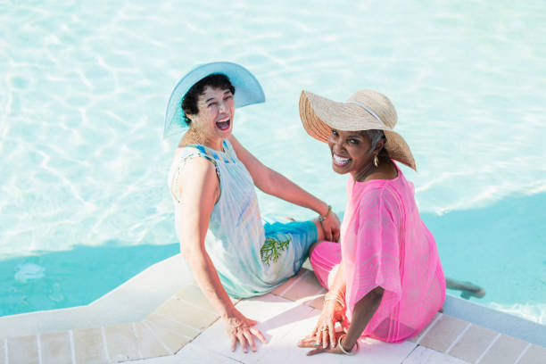 dos senior femenino sentado en la terraza de la piscina, pies en el agua - swimming pool water people sitting fotografías e imágenes de stock