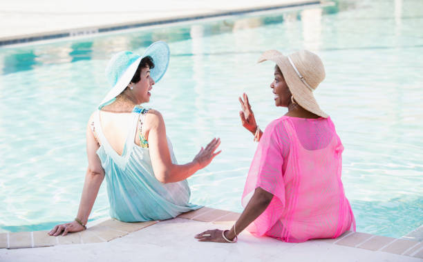 istock Two senior women sitting on pool deck, feet in water 1128249176