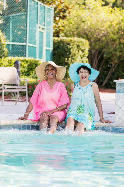 istock Two senior women sitting on pool deck, feet in water 1128249306