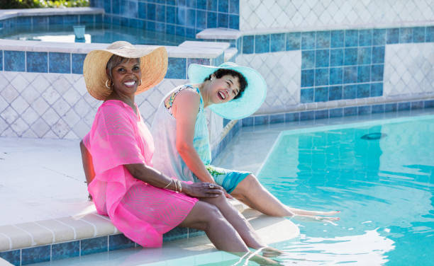 istock Two senior women sitting on pool deck, feet in water 1128249382