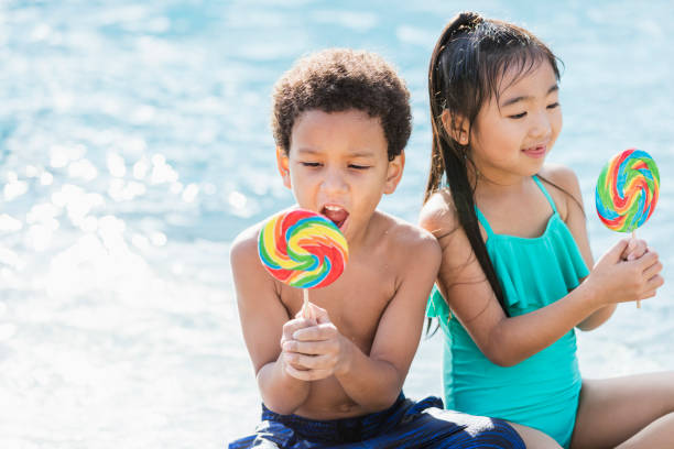 istock Two multi-ethnic children sitting by pool with lollipops 1128250487
