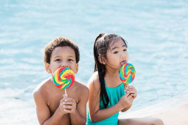 istock Two multi-ethnic children sitting by pool with lollipops 1128250622